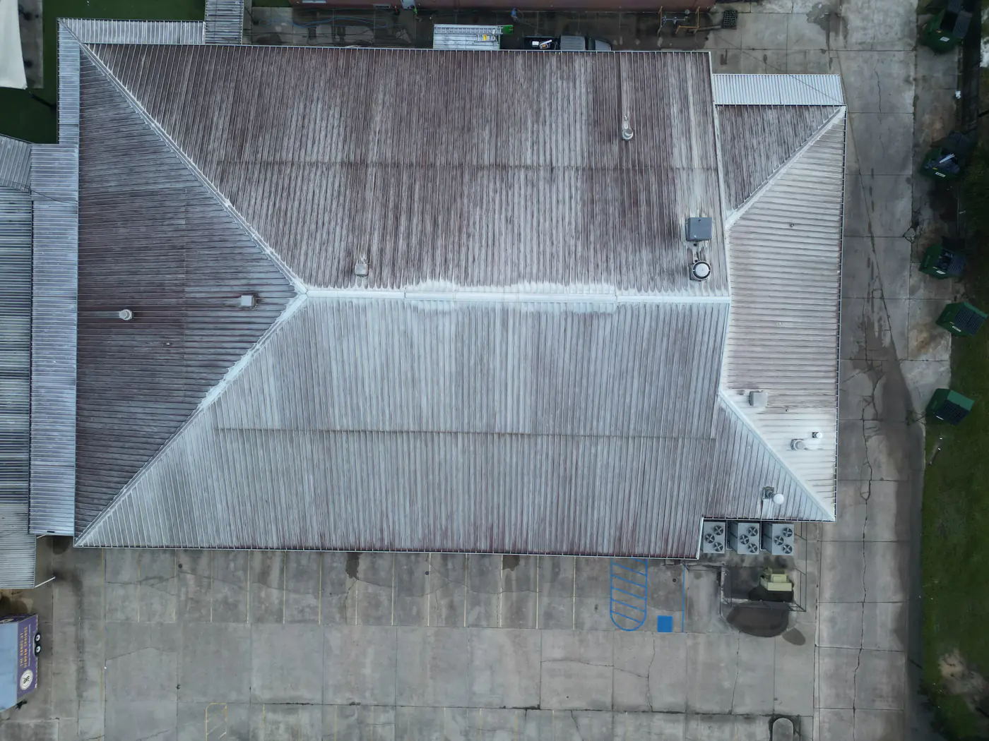 Aerial view of a large commercial metal roof with heavy rust and grey streaking before cleaning.