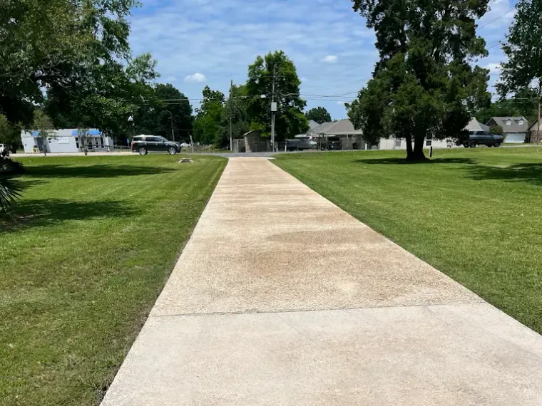A long residential concrete driveway after cleaning, running from the street between wide lawns.