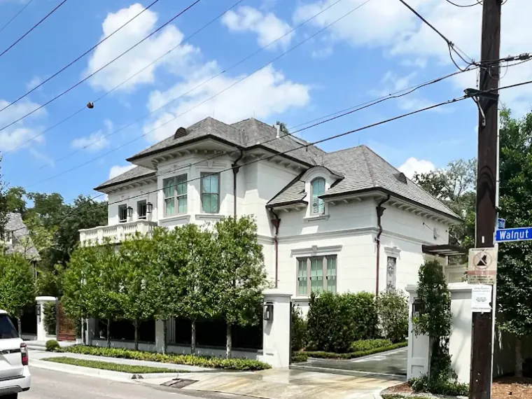 A large white stucco home on a corner lot after a house washing, the exterior cleaned to a uniform bright white.